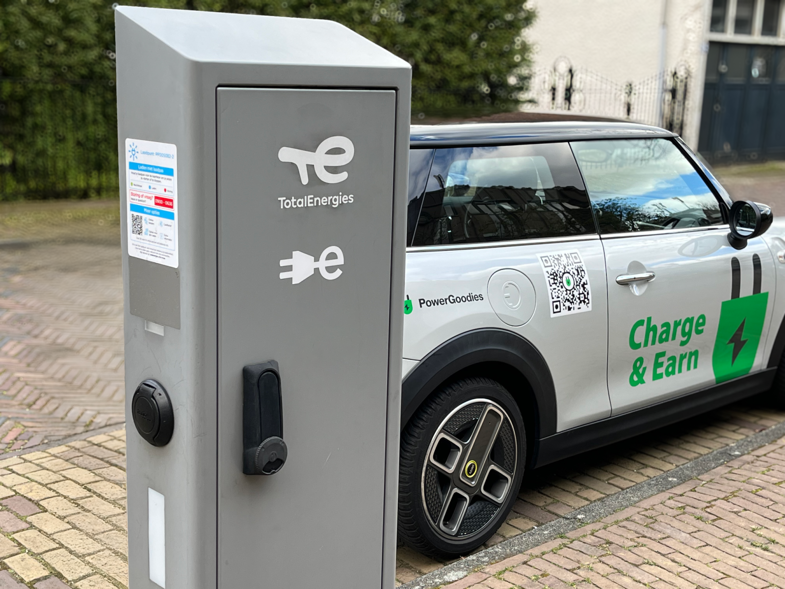 Coche eléctrico con el rótulo Charge & Earn cargando en un punto de carga TotalEnergies con PowerGoodies
